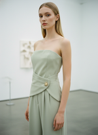 Woman wearing a strapless light green dress with a belt in a minimalistic setting
