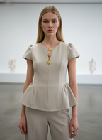 Woman wearing a beige peplum top with gold buttons in a minimalistic setting
