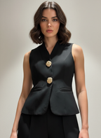 Woman wearing a black sleeveless blazer with gold buttons on a neutral background