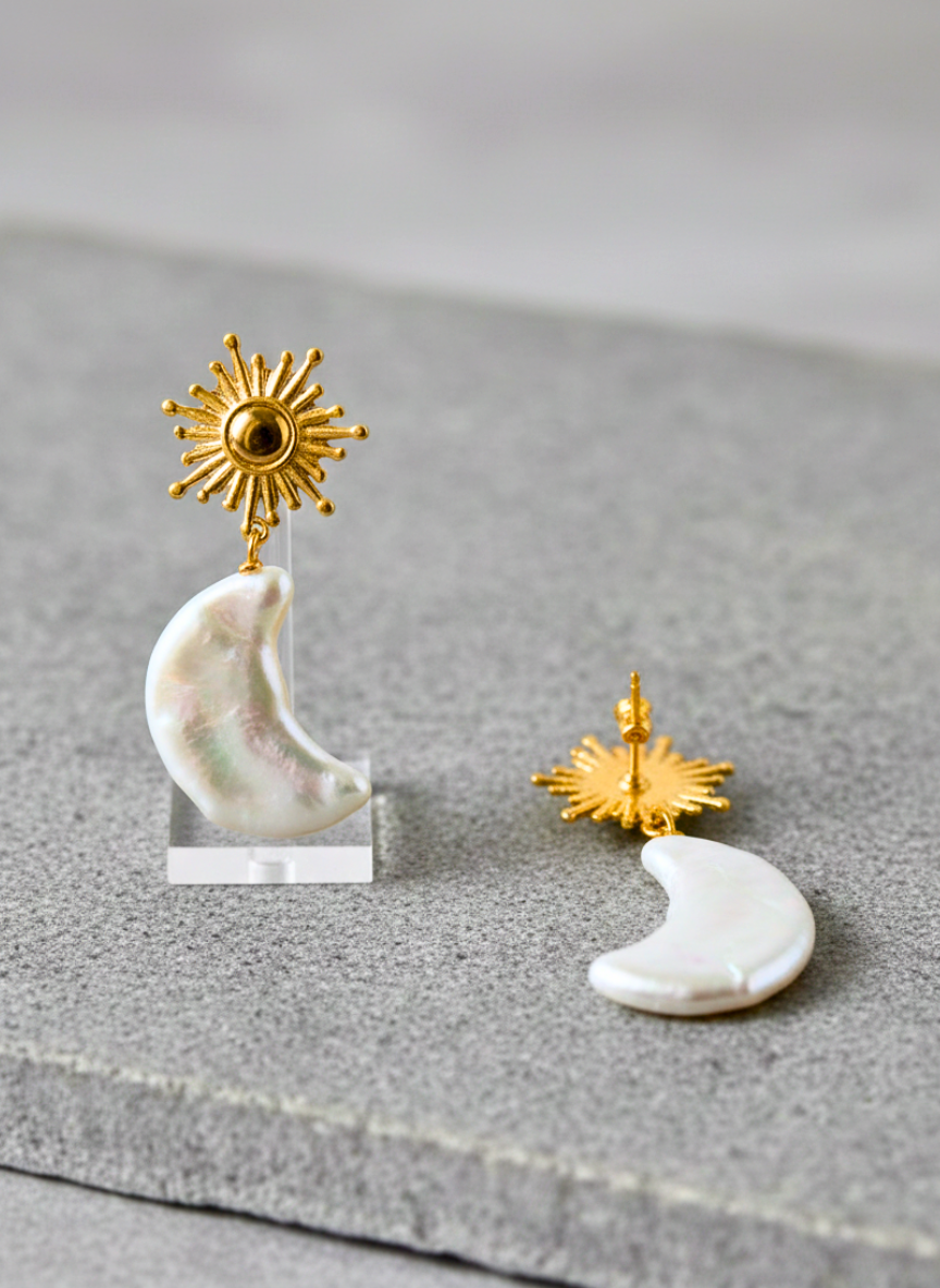 Pair of earrings with gold sun and moon designs on a gray surface