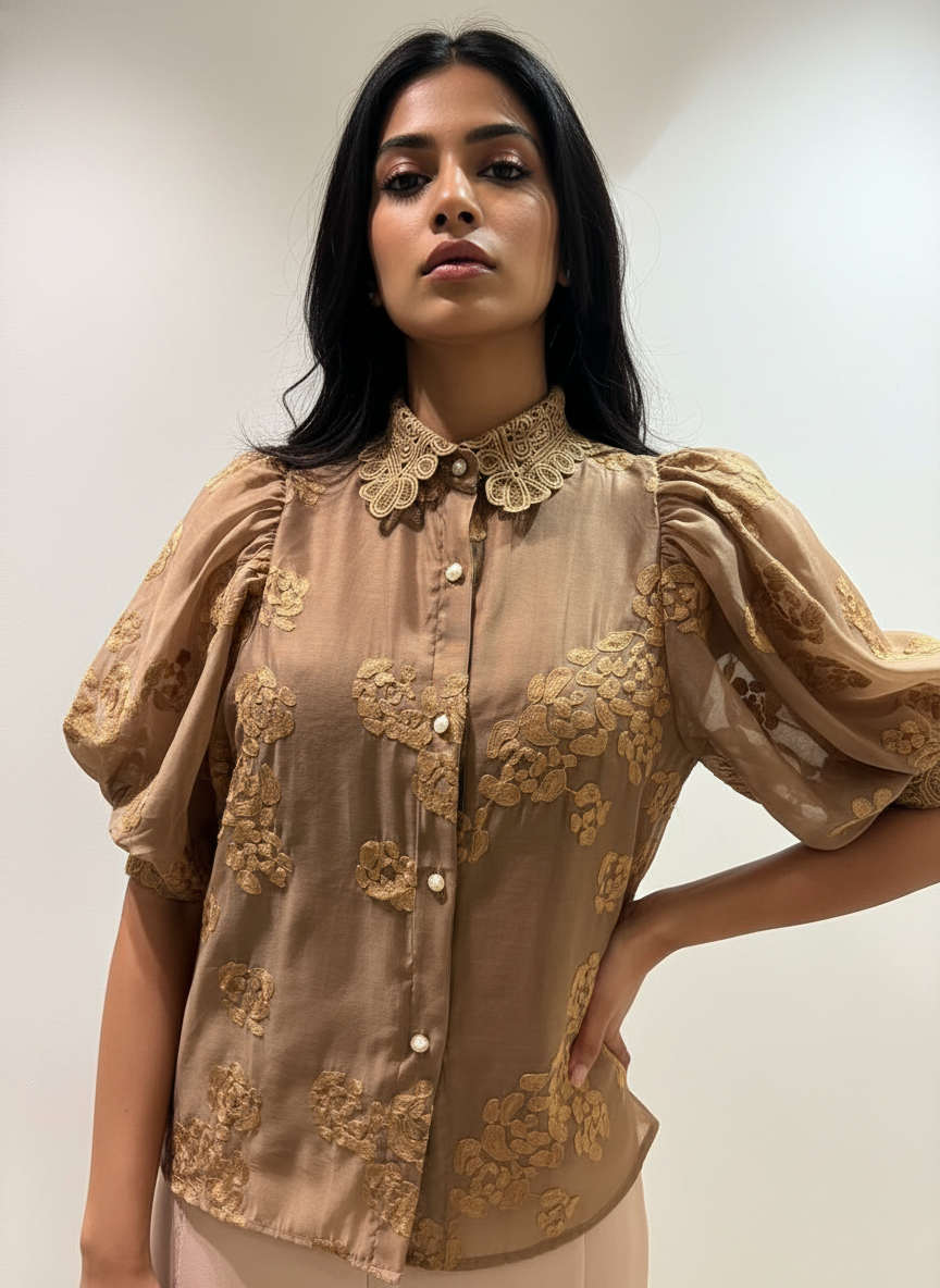 Woman wearing a beige blouse with floral embroidery against a plain background