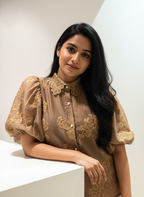 Woman wearing a brown dress with gold embroidery against a white background