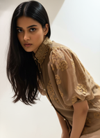 Woman wearing a beige embroidered blouse against a neutral background