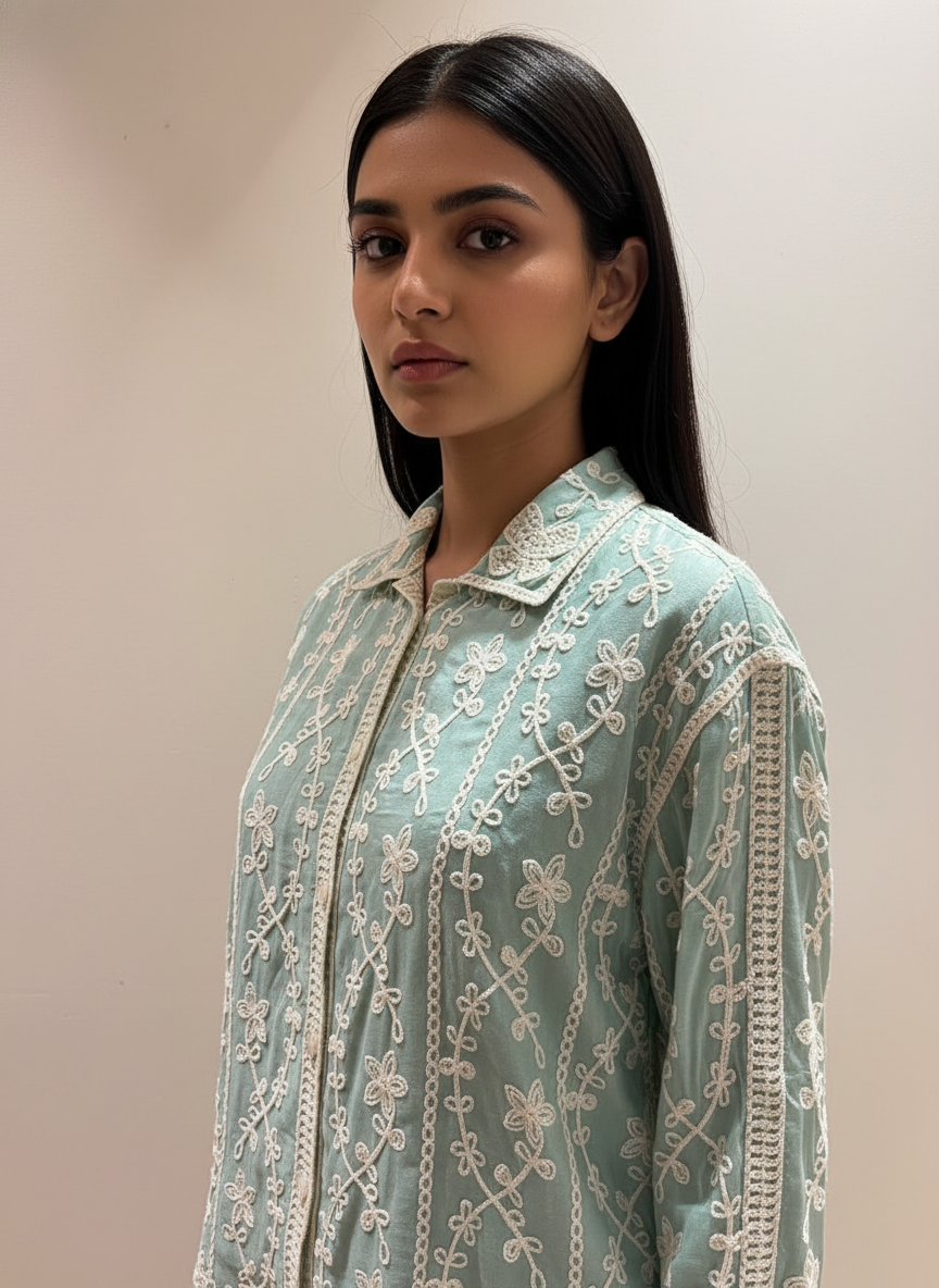 Woman wearing a light blue embroidered traditional outfit against a plain background