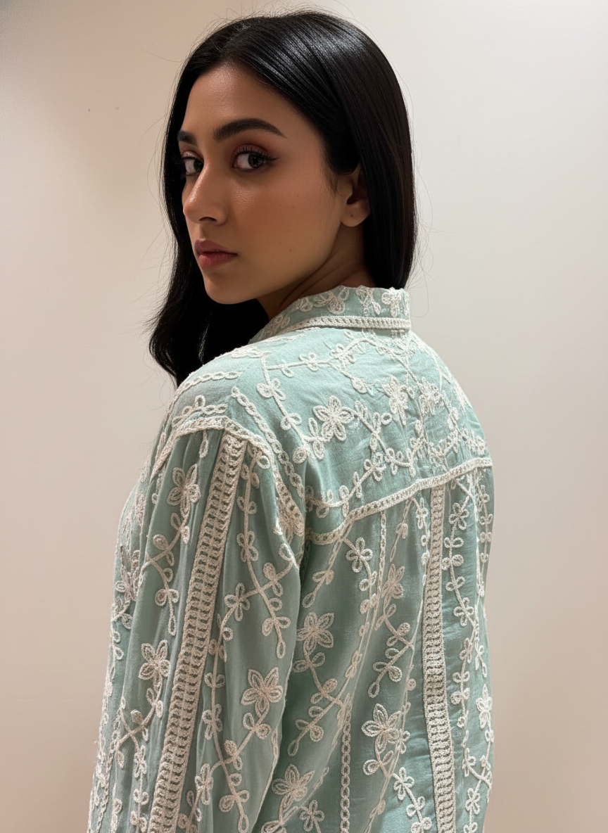 Woman wearing a light blue embroidered traditional outfit against a plain background