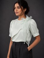 Woman wearing a light green blouse with ruffled details against a dark background