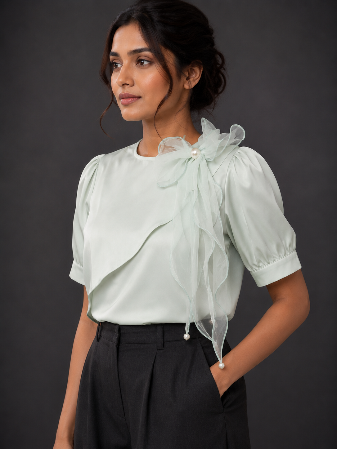Woman wearing a light green blouse with ruffled details against a dark background