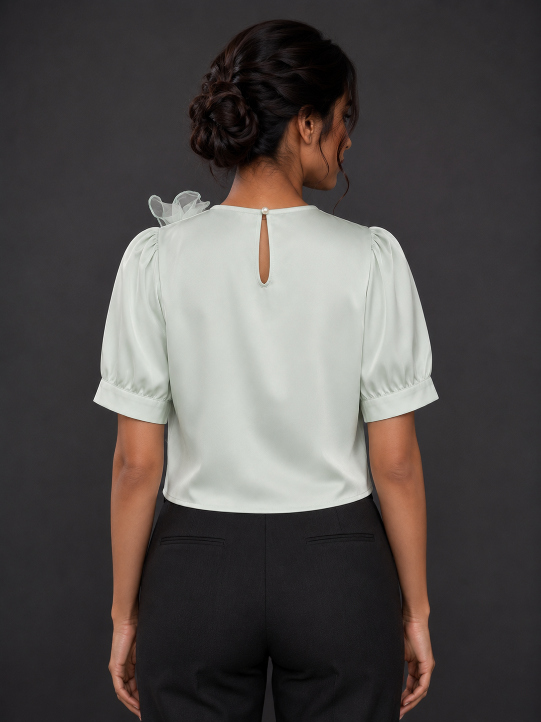 Woman wearing a light green blouse with puffed sleeves and black pants against a dark background