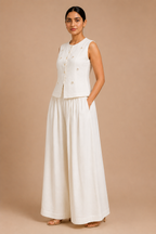 Woman wearing a white sleeveless top and long skirt against a beige background