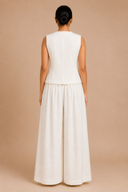Woman wearing a white sleeveless top and wide-leg pants on a beige background