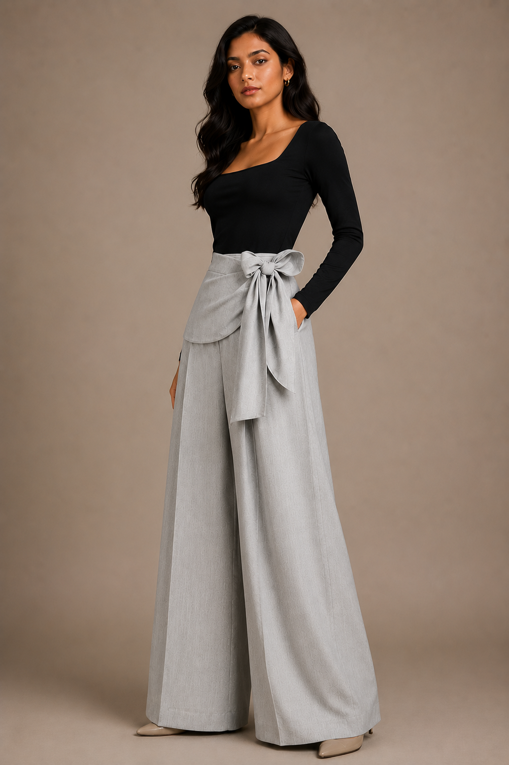 Woman wearing a black top and light gray wide-leg pants with a belt against a beige background