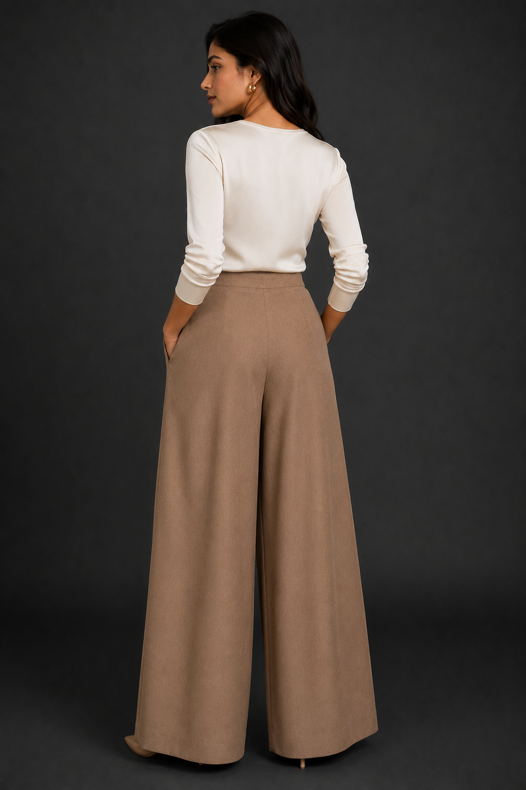 Woman wearing a white long-sleeve top and beige wide-leg pants against a dark background