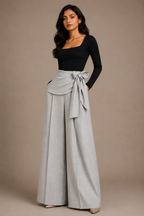 Woman wearing a black top and light gray wide-leg pants with a belt against a beige background