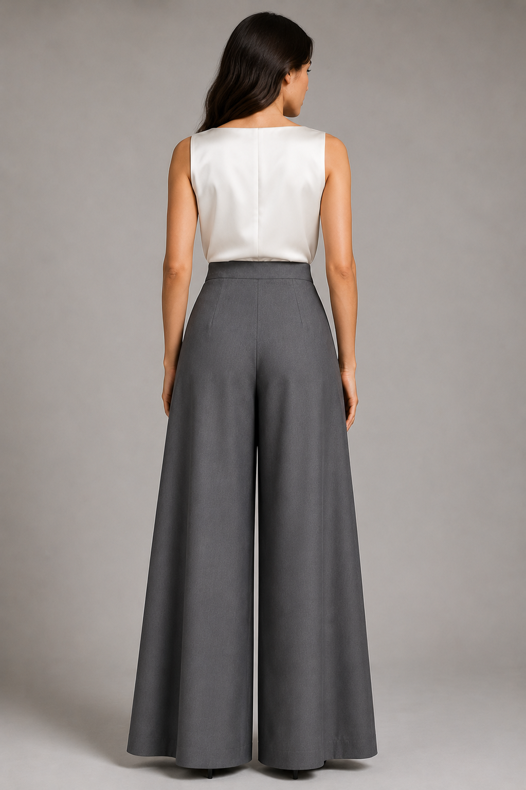 Woman wearing a white sleeveless top and gray wide-leg pants on a plain background