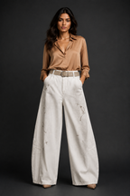 Woman wearing a beige blouse and white pants with embroidery on a black background