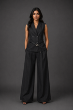 Woman wearing a black vest and wide-leg pants against a gray background