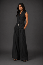 Woman wearing a black sleeveless blazer and wide-leg pants against a dark background