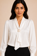 Woman wearing a white blouse with a decorative clasp on a beige background