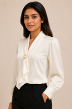 Woman wearing a white blouse with a tie detail against a beige background