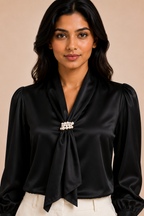 Woman wearing a black blouse with a decorative brooch against a beige background