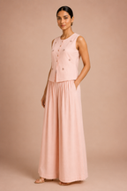 Woman wearing a pink sleeveless top and long skirt against a beige background