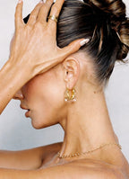 Close-up of a person wearing gold earrings and a necklace with a plain background