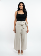 Woman wearing a black top and beige wide-leg pants with a tie waist on a white background
