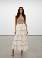 Woman wearing a beige top and white tiered skirt against a plain background