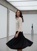 Woman in a white lace top and black skirt standing in a modern indoor setting.